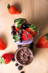 fruits strawberries and blueberries with chocolate topping in a glas wooden background