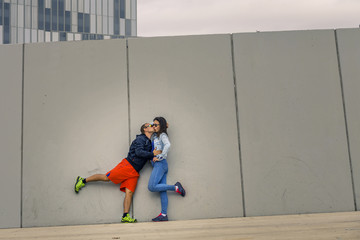 Portrait of young and attractive couple standing in front of the wall in urban park of Barcelona, Spain. They are kissing each other.