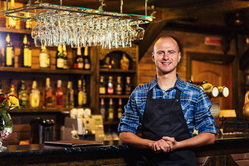 Barman at work in pub,Portrait of cheerful barman worker standing,Waiter giving menus,A pub.Bar.Restaurant.Classic.Evening.European restaurant.European bar.American restaurant.American bar.