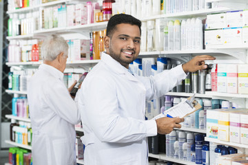 Smiling Chemist Counting Stock With Colleague In Pharmacy