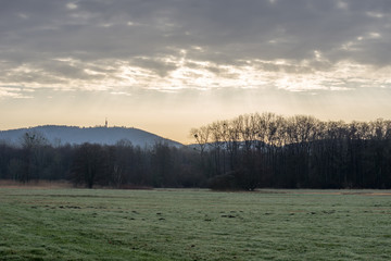 Fototapeta premium Meadow and forest with mountain Fremersberg in the background and sky with sunbeams