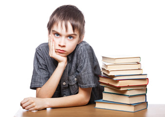 Portrait of frustrated schoolboy sitting at a desk with pile of books holding his head having learning problems