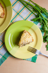 Piece of pancakes pie with mushrooms and chicken meat on green plate and metal fork. Traditional meal for Maslenitsa - Russian pancake week..