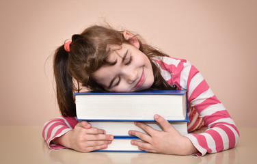 Smiling young girl with closed eyes sitting at the table with her head on the books