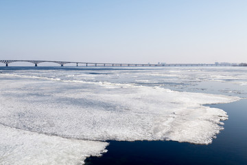 The spring ice drift on the river Volga. Road bridge in the city of Saratov. Russia. A Sunny day in March. Blue sky.