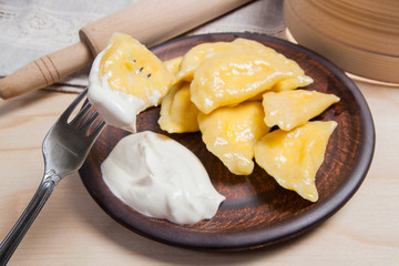 Close up view of boiled varenyky or dumpling with cottage cheese or curd on metal fork. Fresh boiled homemade ukrainian dumplings on clay plate and with sour cream on wooden background..