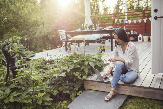 High angle view of woman using laptop while sitting on floorboard at patio in back yard