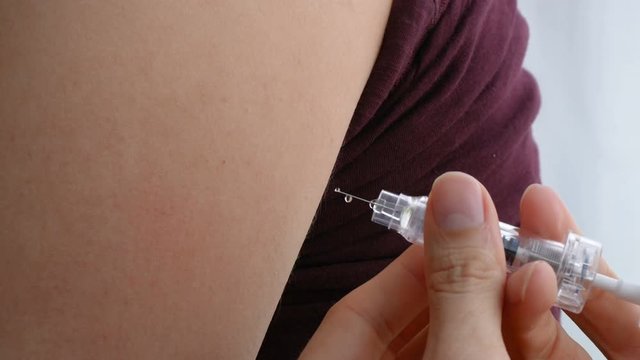 Closeup of giving an intramuscular anticoagulant injection into the arm using a safety syringe.