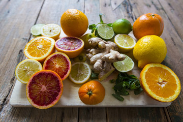 Sliced and whole lemons, oranges and limes, ginger root and mint leaves on wooden board