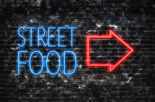 Street food neon sign with arrow on dark brick wall