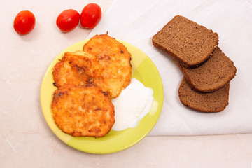 Potato pancakes with meat and tomatoes on green plate with rye black bread in Belarusian style on light background.
