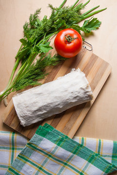Pita bread or lavash wrapped with cottage cheese or curd, chicken, tomatoes and herbs - dill, onion, parsley on cutting board..