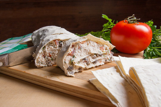 Pieces of cutted pita bread or lavash roll with cottage cheese or curd, chicken, tomatoes and herbs - dill, onion, parsley with intige knife on cutting board..