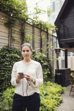 Portrait of confident businesswoman holding smart phone at office yard