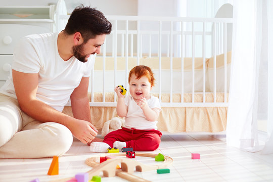 happy father playing with infant baby boy at sunny nursery room