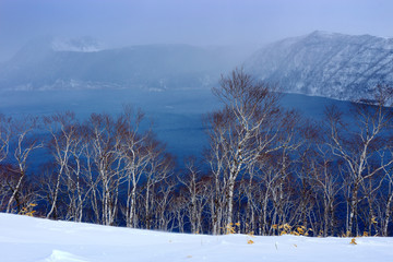 Lake Mashu, endorheic crater lake formed in the caldera of a potentially active volcano,  Akan National Park Volcano, Hokkaido, Japan. Winter scene with snow. Lake with trees in the crater.