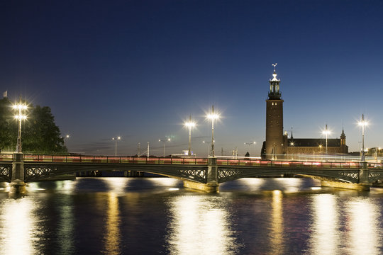 Illuminated Vasabron bridge over Lilla Vartan with Stockholm City Hall against sky at night