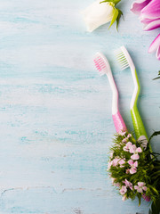 Two pastel toothbrushes with flowers herbs over green textured background. Spring colors. Personal dental health care. Healthy couple concept