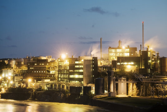 Illuminated factory by river against sky at night