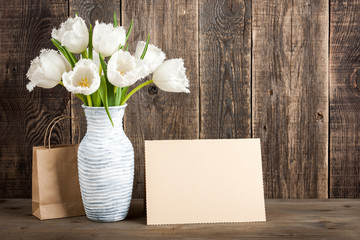 Fresh white tulips bouquet in jug, gift bag