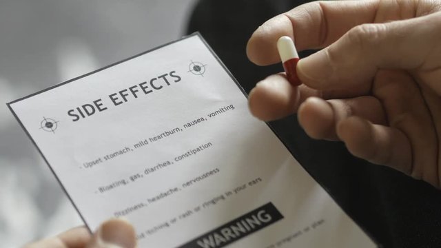 holding a side effect warning documentation paper and a medical pill.