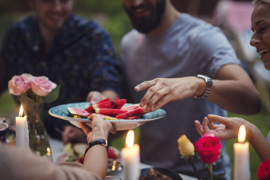 Cropped image of woman serving watermelon slices to friends at garden party