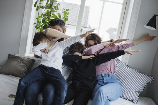 Cheerful family doing dab while sitting on sofa in living room at home