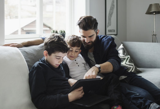 Father and sons using tablet while sitting on sofa at home