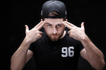 portrait of handsome young man in black shirt and cap on black background. rapper