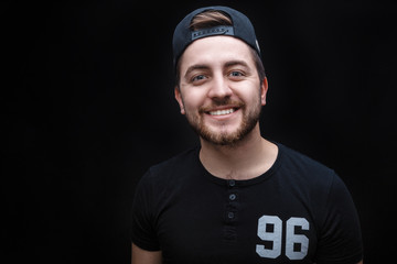 portrait of young attractive smiling brunette man in black hat on black background.