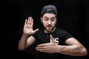 portrait of young man in shirt and cap on black background makes the hand trick
