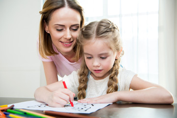 Happy mother and cute little daughter drawing at table