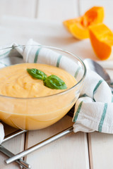 Pumpkin cream soup with basil and pumpkin slice on wooden background