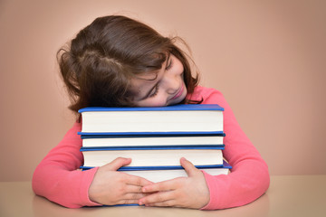 Tired young girl sitting and sleeping at the table with her head on the books