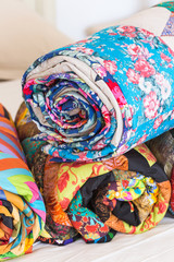 Three colored patchwork quilts twisted into close up. Colorful scrappy blankets folded as background. Handmade. DOF.