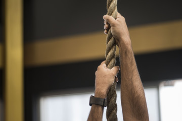 closeup of Man's hairy arms grasping or holding a rope indicating someone climbing in a gym blurred...