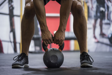 Fototapeta na wymiar Legs and arms of man holding a kettlebell in a cross fit gym with a blurred background 