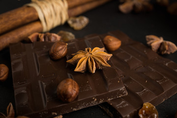 Dark chocolate bar with nuts and spices on the black wooden background