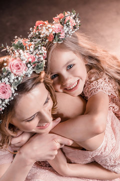 portrait of happy hugging daughter and mother in flowers wreathes