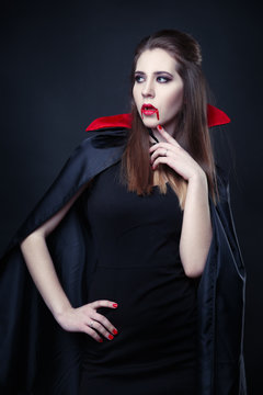 Portrait of a beautiful vampire girl in a cloak of dracula.