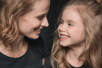 portrait of stylish daughter and mother smiling and looking at each other on black