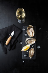 Fresh oysters with lemon and a glass of wine on a dark background