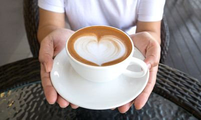 Hands holding a cup of hot latte cappuccino heart shape foam coffee