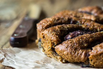 Vegan eggless whole wheat plum cake on parchment paper, knife, wood kitchen table, close up, rustic style