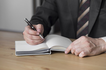 a man in a white shirt and a suit with a pen in his hand writing in a notebook. businessman. pen in hand
