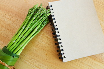 Bundle of fresh asparagus on wooden background and blank diary book.