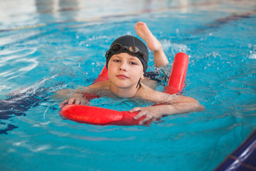 boy  swimming with a red foam noodle in a indoor pool