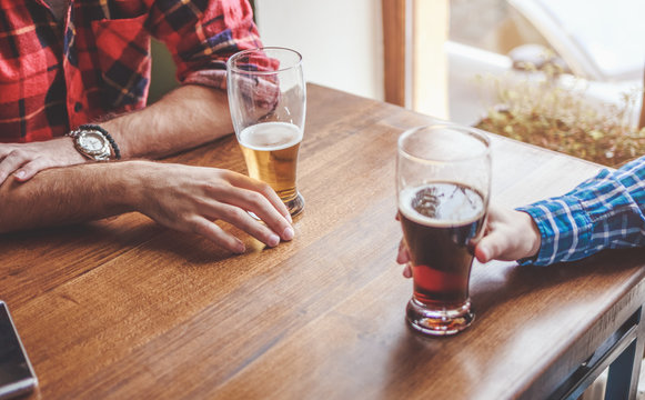 Hands holding glasses with beer on a table.