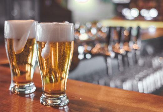 Two  Glasses Of Beer On A Bar Table. Beer Tap On Background