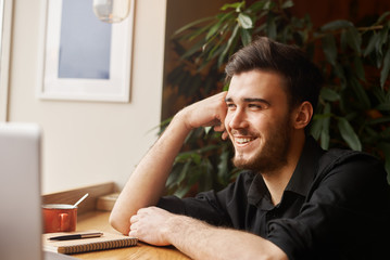 Handsome bearded hipster in black shirt sit in cafe with notebook and talk in the internet. Man...